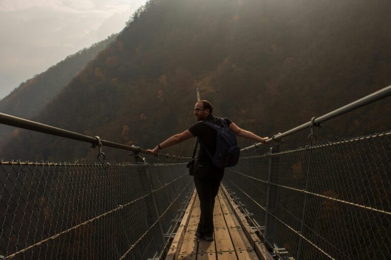 A man with a backpack crossing a suspension bridge in a foggy mountain setting.