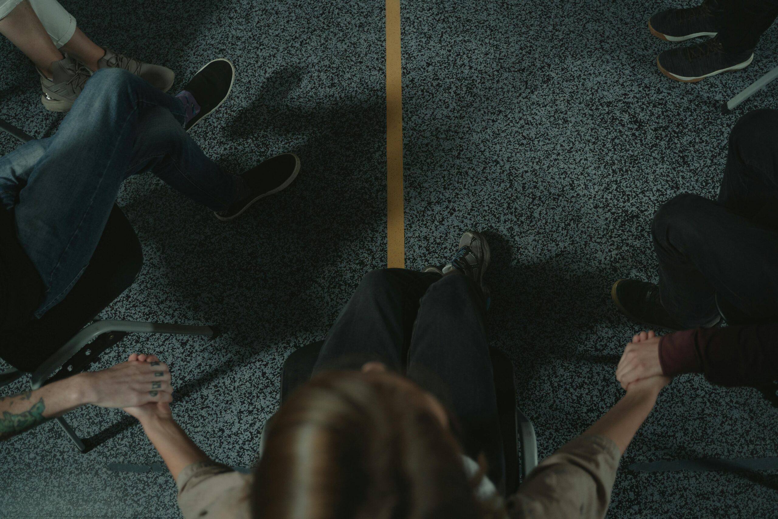 A diverse group of people holding hands in a circle, symbolizing support and unity in a mental health session.